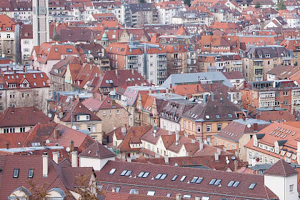 Blick von schräg oben über ein Häusermeer aus Altbauten, am Rand erhebt sich ein moderner Kirchturm über die Häuser